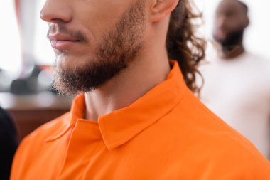 partial view of bearded man in jail uniform near african american juror on blurred background clipart