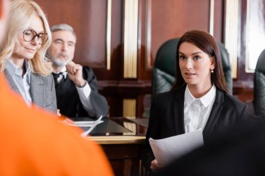 blonde advocate smiling near prosecutor and senior judge on background clipart