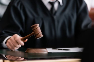 partial view of blurred judge in robe holding gavel in court clipart