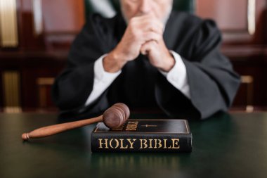 selective focus of bible and gavel near cropped judge on blurred background clipart