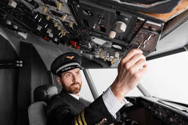 pilot in cap and uniform reaching overhead panel in airplane simulator