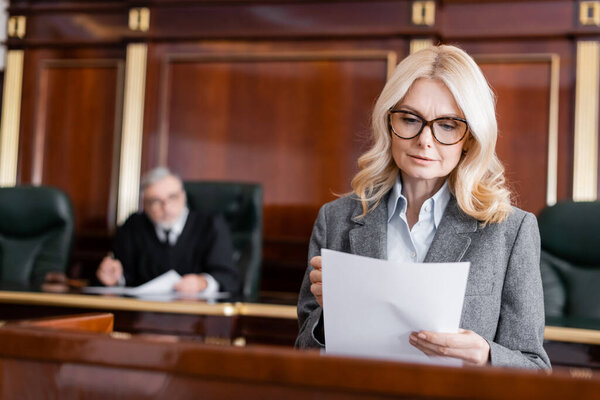 адвокат средних лет в очках, читающий документ во время выступления в суде