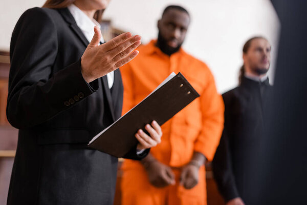 prosecutor with clipboard pointing with hand near accused african american man on blurred background