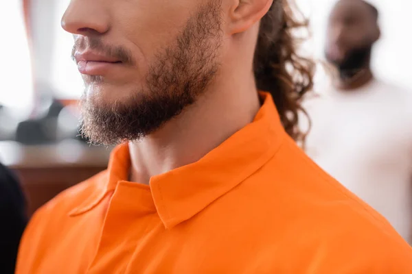 partial view of bearded man in jail uniform near african american juror on blurred background