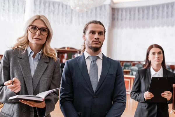 accused businessman standing near advocate and prosecutor in court