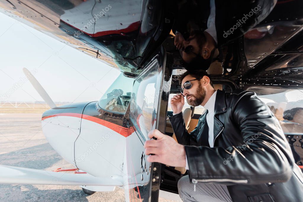 bearded pilot adjusting stylish sunglasses and opening door in helicopter 