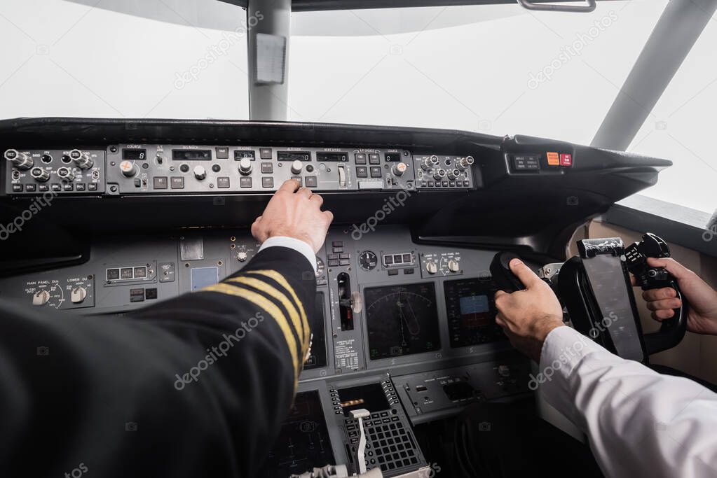 cropped view of pilot reaching control panel near co-pilot using yoke in airplane simulator 