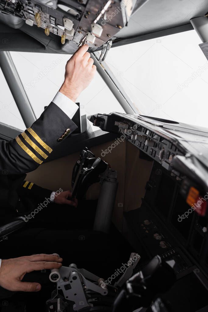 cropped view of pilot in uniform reaching overhead panel near co-pilot using thrust lever in airplane simulator