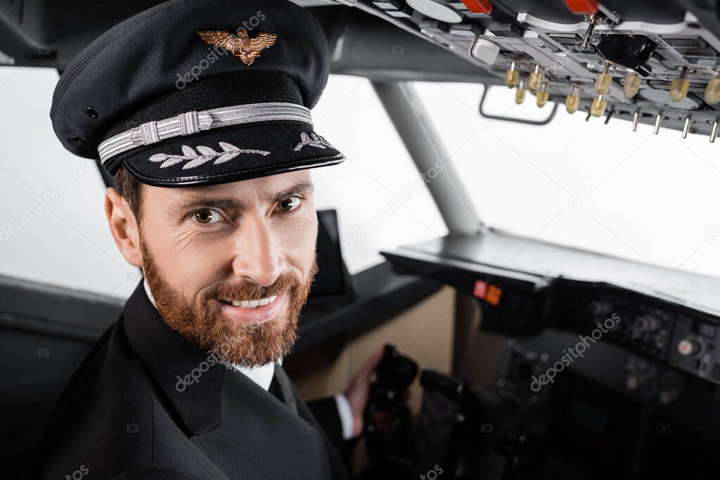 cheerful pilot in cap looking at camera in airplane simulator 