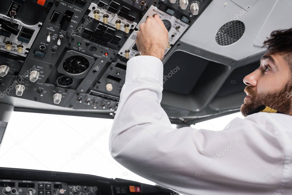 bearded pilot pressing button on overhead panel in airplane simulator