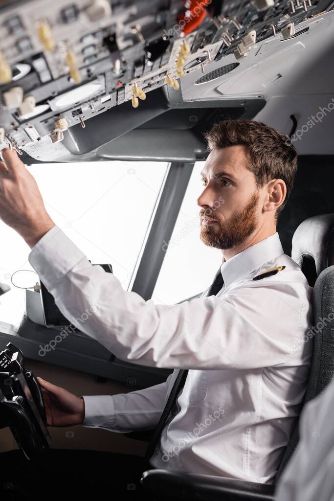 bearded pilot reaching overhead panel while using yoke in airplane simulator