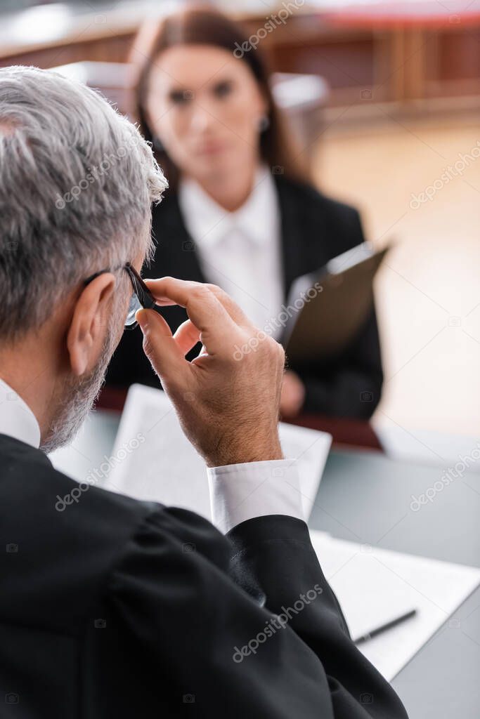 grey-haired judge adjusting eyeglasses near blurred prosecutor in court