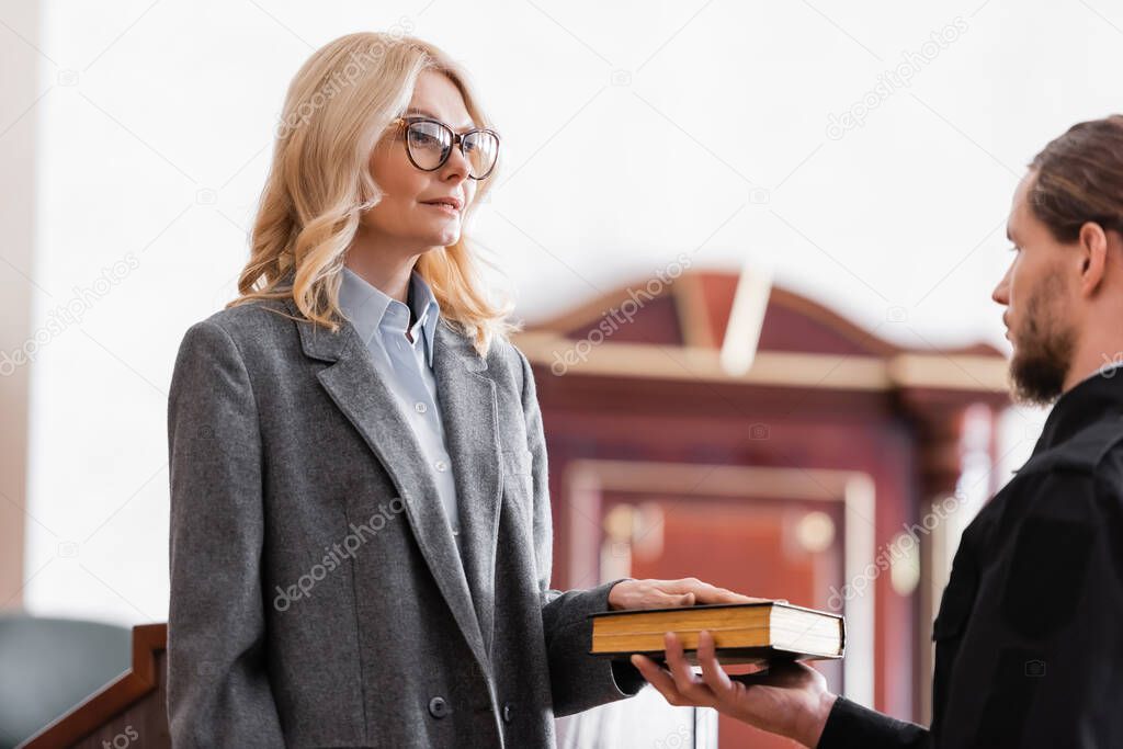 middle aged woman in eyeglasses giving oath on bible in court