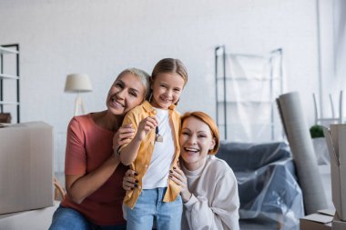 Yeni dairede elinde anahtar olan genç bir kız ve aynı cinsiyetten mutlu bir aile.