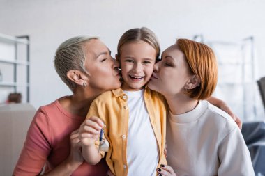 same sex couple kissing happy adopted daughter holding key from new apartment clipart