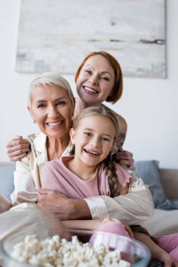 Pijamalı gülümseyen kadın yatak odasında patlamış mısırın yanında sevgilisine ve çocuğuna sarılıyor. 