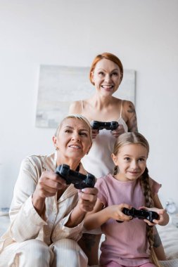 KYIV, UKRAINE - 8 Aralık 2021: Pijamalı kadın ve kızı yatak odasında video oyunu oynuyorlar 