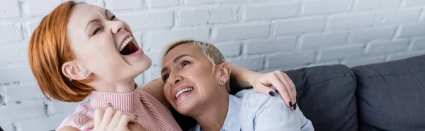 兴奋的女人紧闭双眼 在家里笑着接近同性恋女朋友 高举横幅 — 图库照片