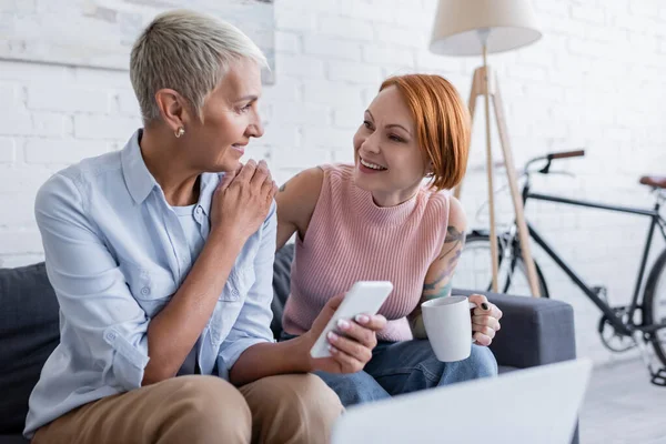 Mujeres Lesbianas Sonrientes Con Taza Teléfono Inteligente Hablando Sofá Casa — Foto de Stock