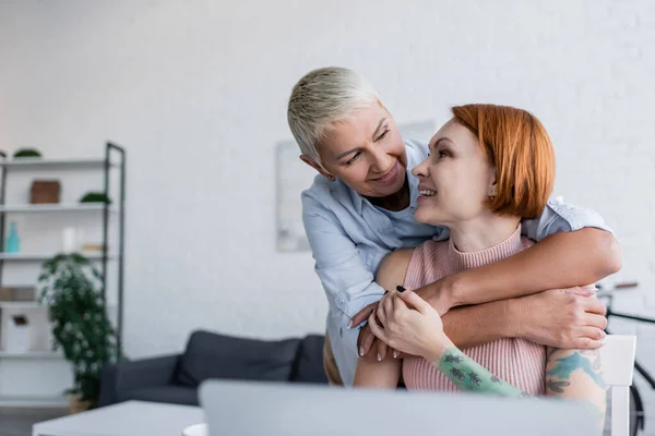 Lesbisk Kvinna Omfamnar Lycklig Tatuerad Flickvän Vardagsrummet — Stockfoto