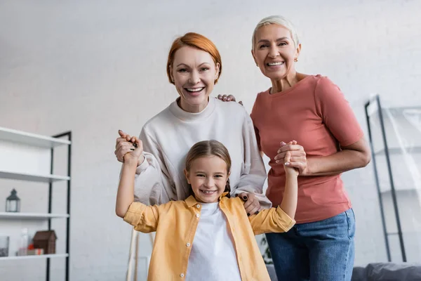 Joyful Lesbian Couple Holding Hands Adopted Daughter Smiling Camera Home — Stock Photo, Image