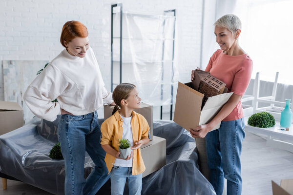 woman holding carton box with house model near adopted daughter and lesbian girlfriend