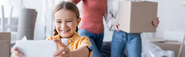 Niño Sonriente Tomando Selfie Cerca Madres Borrosas Con Caja Cartón — Foto de Stock