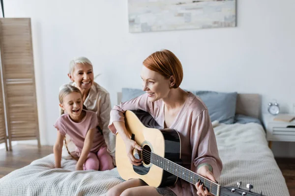 Mujer Feliz Tocando Guitarra Acústica Cerca Borrosa Niño Novia Cama —  Fotos de Stock