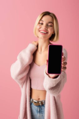 Bulanık ve mutlu genç kadın pembe üzerine izole edilmiş beyaz ekran akıllı telefon tutuyor. 