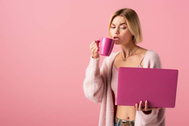 Elinde kahve ve dizüstü bilgisayarı olan pembe bardaklı sarışın kadın. 