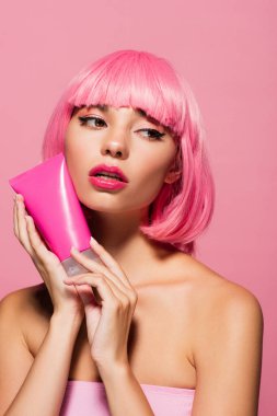 Renkli saçlı genç bir kadın elinde losyonlu pembe bir tüp tutuyor. 