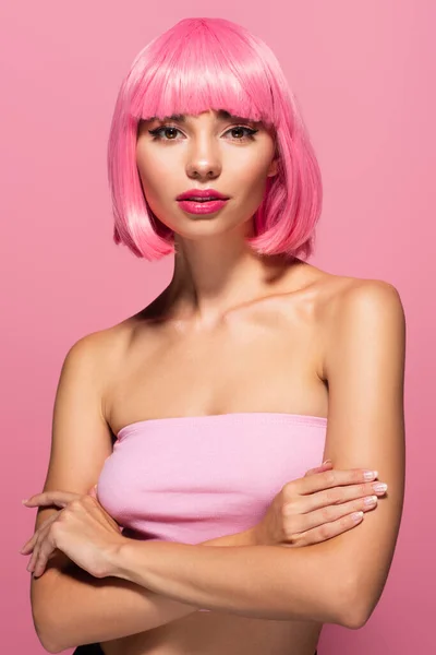 young woman with colored hair and bangs standing with crossed arms isolated on pink