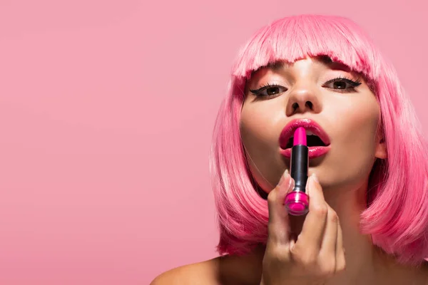 young woman with colored hair and bare shoulders applying lipstick isolated on pink