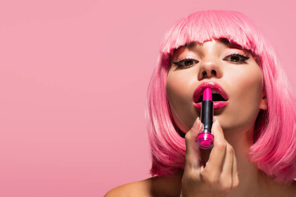 young woman with colored hair and bare shoulders applying lipstick isolated on pink 