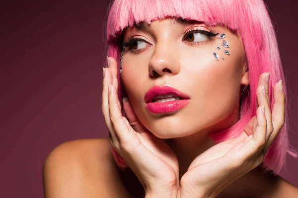 young woman with pink hair and shiny stones on face looking away on dark purple