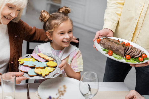 happy family serving table with traditional cookies and meat with vegetables for easter celebration