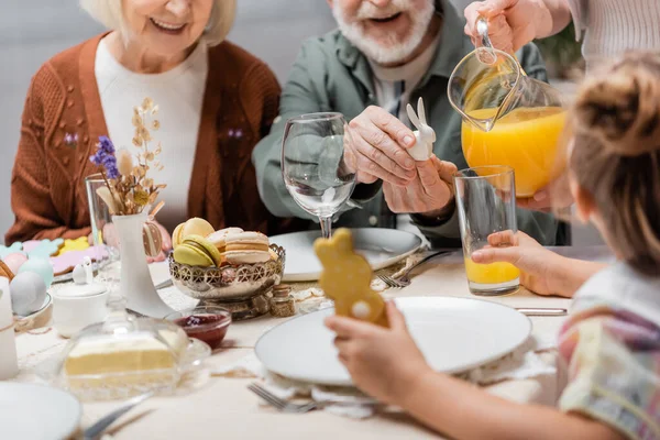 Vista Recortada Mujer Vertiendo Jugo Naranja Cerca Familia Teniendo Cena — Foto de Stock