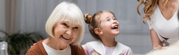 excited girl near smiling granny and mother at home, banner