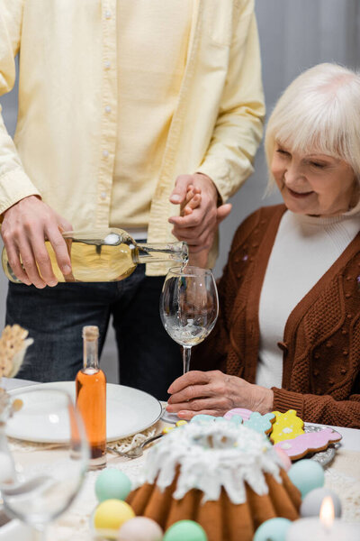 man pouring wine while holding hand of senior mother during easter dinner