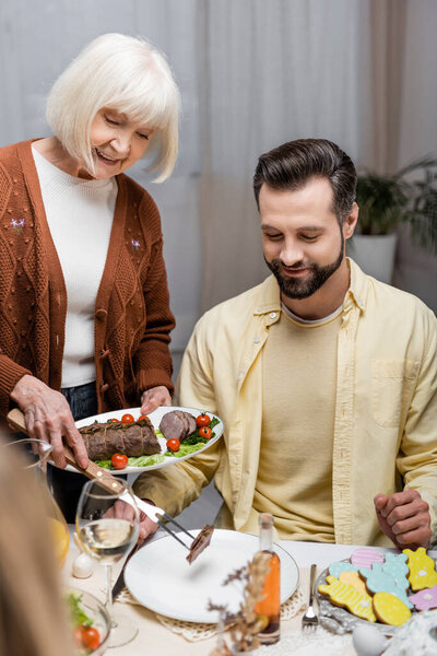senior woman serving fried meat during easter dinner with adult son