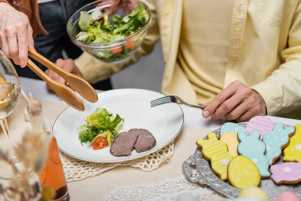 年长妇女在成年儿子身边端着炖菜和蔬菜沙拉的偏视 — 图库照片