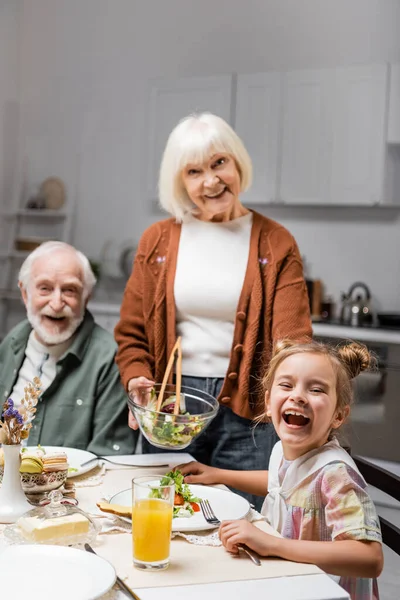 Senior Woman Holding Vegetable Salad Cheerful Husband Laughing Granddaughter — Stock Photo, Image