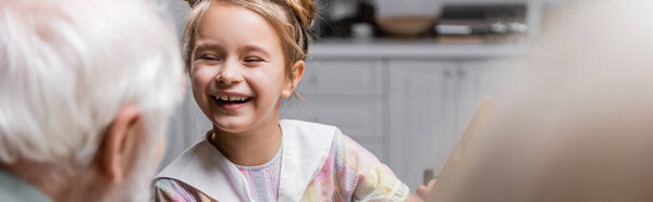 preteen girl smiling ner blurred grandparents at home, banner
