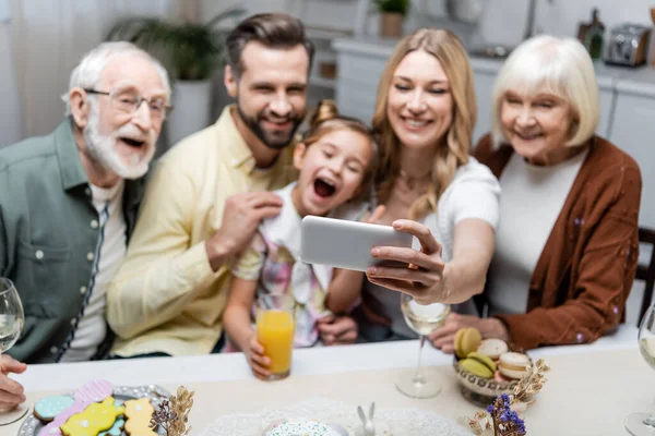 Mujer Tomando Selfie Teléfono Inteligente Con Familia Borrosa Durante Cena —  Fotos de Stock