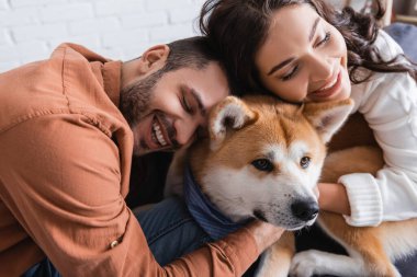 happy young couple hugging akita inu dog at home clipart