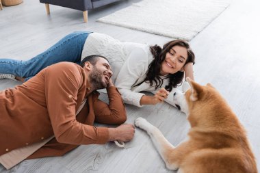 Genç bir çift Akia Inu köpeğiyle gülüyor ve yerde yatıyor.