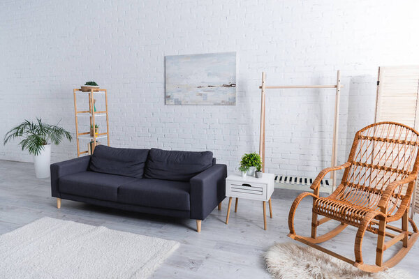 modern living room with sofa, green plants and rattan rocking chair 