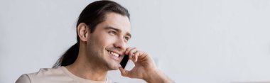 Uzun saçlı mutlu adam akıllı telefondan, afişten konuşuyor.