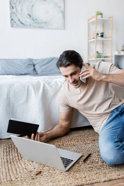 Hombre Sosteniendo Portátil Hablando Teléfono Inteligente Cerca Computadora Portátil Dormitorio —  Fotos de Stock