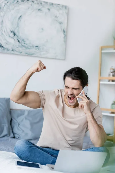 Hombre Emocionado Hablando Teléfono Móvil Cerca Computadora Portátil Dormitorio —  Fotos de Stock